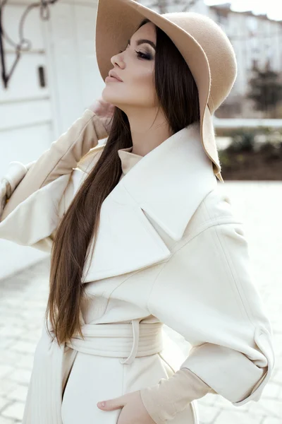 Glamour-Girl mit dunklen glatten Haaren trägt luxuriösen beigen Mantel mit elegantem Hut — Stockfoto