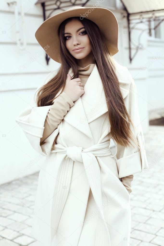 glamour girl with dark straight hair wears luxurious beige coat with elegant hat, 