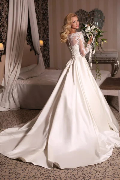 Gorgeous woman with blond hair wears luxurious wedding dress with bouquet — Stock Fotó