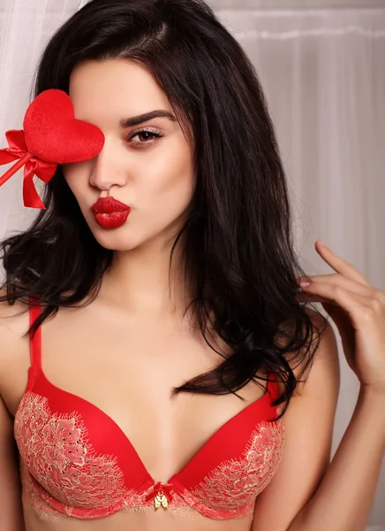 Menina sexy em lingerie de renda elegante, segurando coração vermelho, símbolo do dia dos namorados — Fotografia de Stock