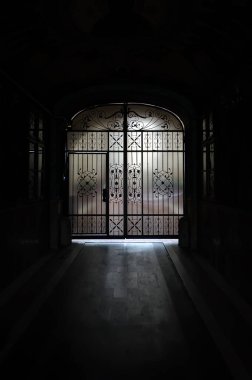 Kapalı kapılı parlak çıkışı olan eski karanlık bir geçit.