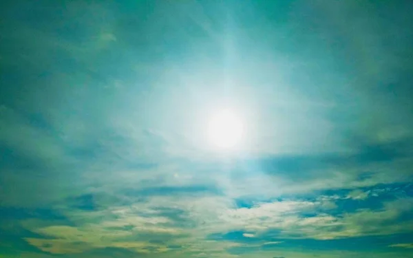Brightly shining sun in the cloudy blue sky, natural background