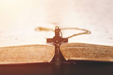  Açık bir İncil 'in ortasına dikey yerleştirilmiş bir haç kolyesi. Hristiyan inancını, fedakarlığını, ibadetini ve bağlılığını simgeliyor. Sıcak ve huzurlu bir aydınlatma atmosferi var..