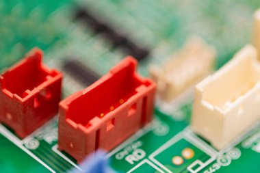 Macro shot of colorful electronic connectors, including red and white plastic sockets, mounted on a green circuit board. The image highlights detailed components used in electrical and electronic systems for connectivity.