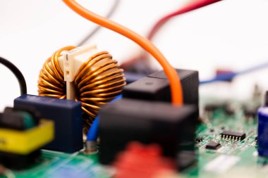 Close-up of a copper coil inductor mounted on a green PCB, surrounded by relays, connectors, and colorful wires, illustrating modern power electronics and circuit design.
