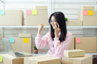 Gülümseyen kadın telefonda dizüstü bilgisayarla ve kutularla konuşurken, e-ticaret iş akışı, iletişim ve küçük işletme verimliliğini ifade ederken çevrimiçi mağaza görevlerini yönetiyor..