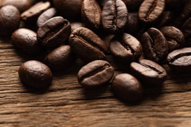 Kavrulmuş kahve çekirdeklerini ahşap masa üzerinde yakın çekimde zengin doku ve koyu kahverengi tonları gösterir.