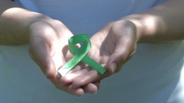 Woman holding green awareness ribbon in hands