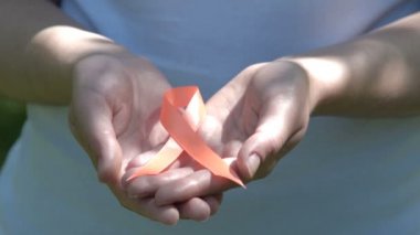 Woman holding orange awareness ribbon in hands