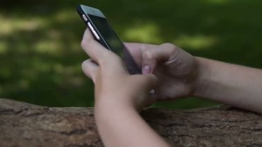 Kız parkta cep telefonuna yazarak