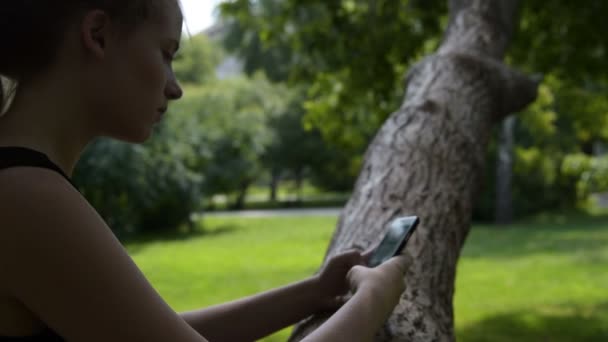 Tonåring flicka surfa webben på mobil i parken — Stockvideo