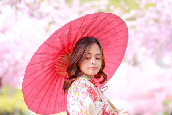 旅行者の肖像若いアジア人女性が浴衣を着て日差しの日の午後に桜公園を開花日本の木の道を歩く — ストック写真