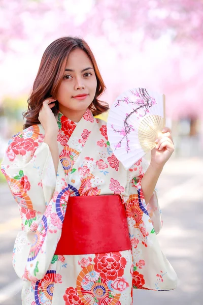 旅行者の肖像若いアジア人女性が浴衣を着て日差しの日の午後に桜公園を開花日本の木の道を歩く — ストック写真