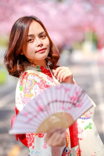 旅行者の肖像若いアジア人女性が浴衣を着て日差しの日の午後に桜公園を開花日本の木の道を歩く — ストック写真