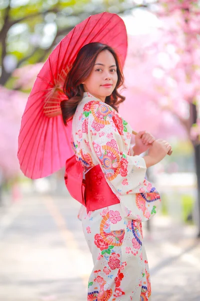 旅行者の肖像若いアジア人女性が浴衣を着て日差しの日の午後に桜公園を開花日本の木の道を歩く — ストック写真