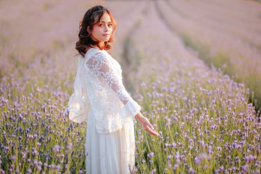 Lavanta tarlasında uzun sarı saçlı bir kadın. Stil hayatı, yaz günlerinde uzun beyaz elbiseli ve rahatlamış bir şekilde seyahatin tadını çıkarır..