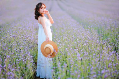 Lavanta tarlasında uzun sarı saçlı bir kadın. Stil hayatı, yaz günlerinde uzun beyaz elbiseli ve rahatlamış bir şekilde seyahatin tadını çıkarır..