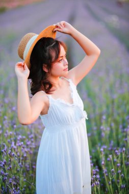 Lavanta tarlasında uzun sarı saçlı bir kadın. Stil hayatı, yaz günlerinde uzun beyaz elbiseli ve rahatlamış bir şekilde seyahatin tadını çıkarır..