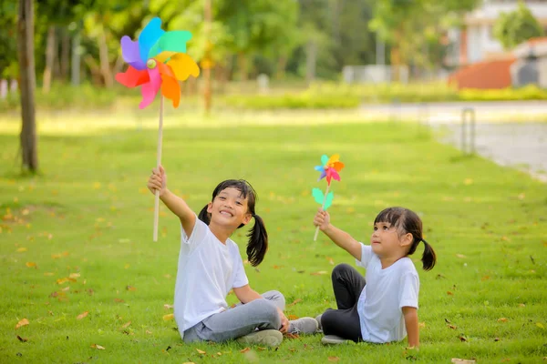 芝生の上でカラフルなおもちゃの風車で遊んでいる2人のかわいい女の子アジア 開発を増加させ 学習スキルを向上させる再生可能エネルギーと持続可能な資源 — ストック写真