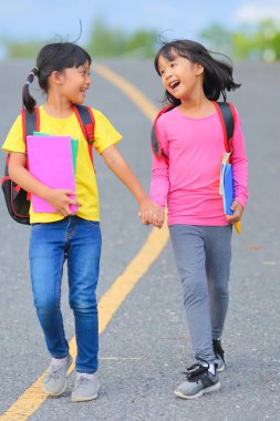 Covid-19 salgınından sonra okula geri döndü. İki küçük tatlı kız okula giderken kollarında kitap tutarak ve çantalarını çantasıyla yürüyüp konuşuyorlardı..