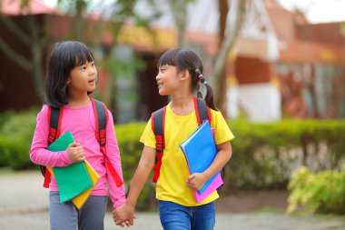 Covid-19 salgınından sonra okula geri döndü. İki küçük tatlı kız okula giderken kollarında kitap tutarak ve çantalarını çantasıyla yürüyüp konuşuyorlardı..