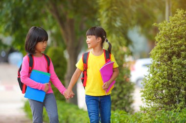 Covid-19 salgınından sonra okula geri döndü. İki küçük tatlı kız okula giderken kollarında kitap tutarak ve çantalarını çantasıyla yürüyüp konuşuyorlardı..