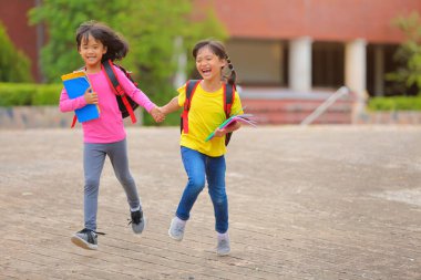 Covid-19 salgınından sonra okula geri döndü. İki küçük tatlı kız okula giderken kollarında kitap tutarak ve çantalarını çantasıyla yürüyüp konuşuyorlardı..