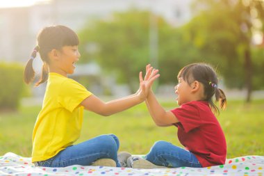 Gülümseyen Asyalı küçük kız parkta doğada oturmaktan mutlu. Bu da sınıfın öğrenme becerilerinin dışında gelişimi ve gelişimi arttırır..