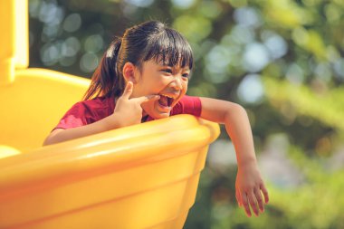 Neşeli, neşeli küçük kız yaz aylarında oyun parkında dolaşır. Açık hava aktivitesi. İnandırıcılık ve dış eğitim konsepti..