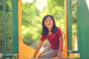 Neşeli, neşeli küçük kız yaz aylarında oyun parkında dolaşır. Açık hava aktivitesi. İnandırıcılık ve dış eğitim konsepti..