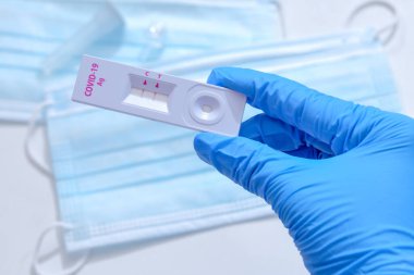 Mavi tıbbi eldiven giyen ve COVID-19 (SARS-CoV-2) kullanan bir kadın, evdeki Hızlı Tespit testine yardımcı olmak için ilk Antijen Test kiti cihazı. Pozitif COVID-19 salgını.