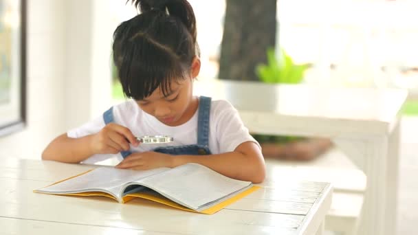 Kot Pantolon Giyen Asyalı Küçük Bir Kız Masada Büyüteçle Kitap — Stok video