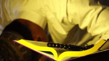 Beyaz elbiseli Müslüman adamın Kur 'an kitabı okuduğu görüntüler.