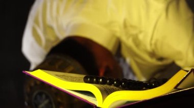 Beyaz elbiseli Müslüman adamın Kur 'an kitabı okuduğu görüntüler.