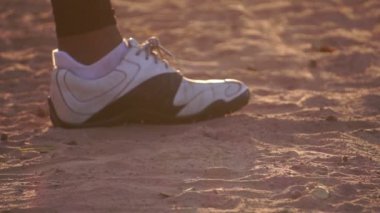Bir beyzbol oyuncusunun ayaklarının yakın çekim görüntüleri ve sıcak ışıkta yerde duran sopa. 