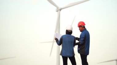 İki mühendis arka planda yel değirmenleriyle planları tartışıyor.
