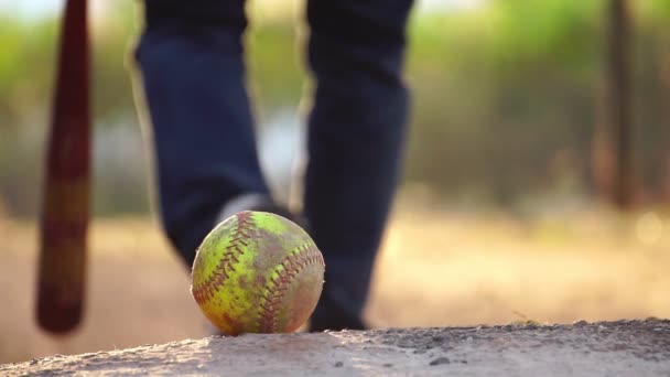 暖かい光の中で地面にボールのクローズアップ映像 背景に野球バットを持つ選手 — ストック動画