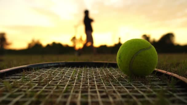 テニスラケットとボールのクローズアップ映像背景にある試合中のぼやけたテニスプレーヤー — ストック動画
