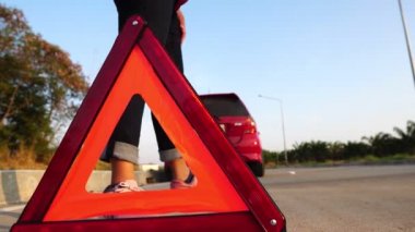 footage of woman putting triangle sign on the road because her car is broken down, red car on the road and woman 