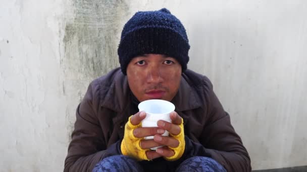 一个男人坐在墙边 手里拿着一个塑料杯向无家可归的流浪汉乞讨的镜头 — 图库视频影像