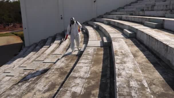 身着防护服 头戴呼吸器 头戴消毒器 在空旷的露天楼梯上行走 在地面上对头颈类动物进行化学消毒的人 — 图库视频影像