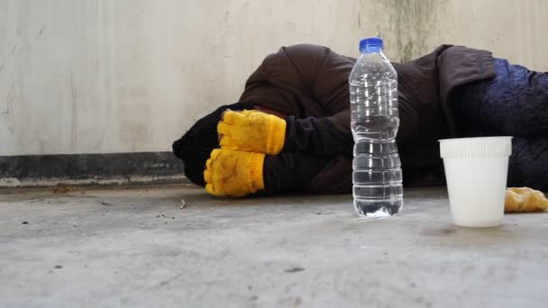 一个男人躺在墙边和水瓶边 面前放着一个装有面包的塑料杯 无家可归的人 流浪汉的镜头 — 图库视频影像