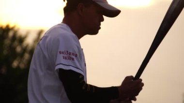 Beyzbol oyuncusunun gün batımında beyzbol sopasıyla topa vuruşunun yavaş çekimleri.