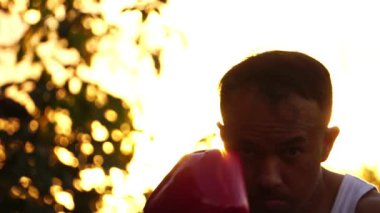  Kırmızı boks eldivenli adam arka planda gün batımında antrenman yapıyor. 