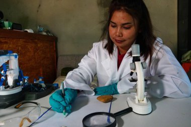 Asyalı kadın mikroskopla kapalı alanda araştırma yapıyor..