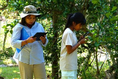 Asyalı kadın araştırmacılar açık hava botanik bahçesinde veri toplamak için tablet kullanıyorlar..