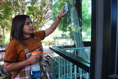 Asyalı bir kadının portresi temizleyici spreyliyor ve pencereyi siliyor.