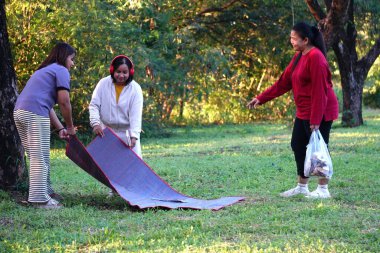 Üç kadın dışarıda piknik battaniyesi kuruyor..