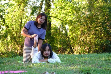 Asyalı kadın gülümsüyor ve masaj için eğiliyor yoga minderinde yüzüstü yatan arkadaşının sırtına..