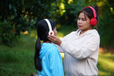 Asyalı kadın açık havada kızlara kulaklık takıyor.